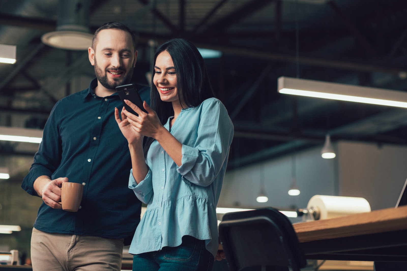 happy-lady-using-modern-smartphone-cheerful-man-standing-by-her-side-with-mug-looking-her-gadget.jpg
